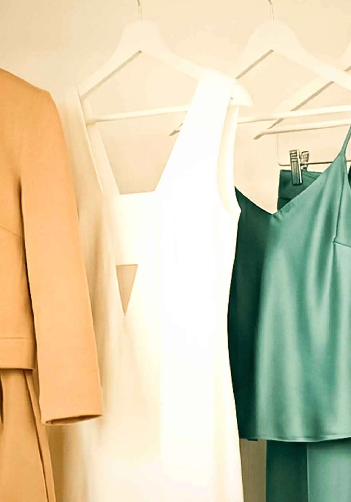 A maxi white dress, a green satin top and more hanging in a closet.