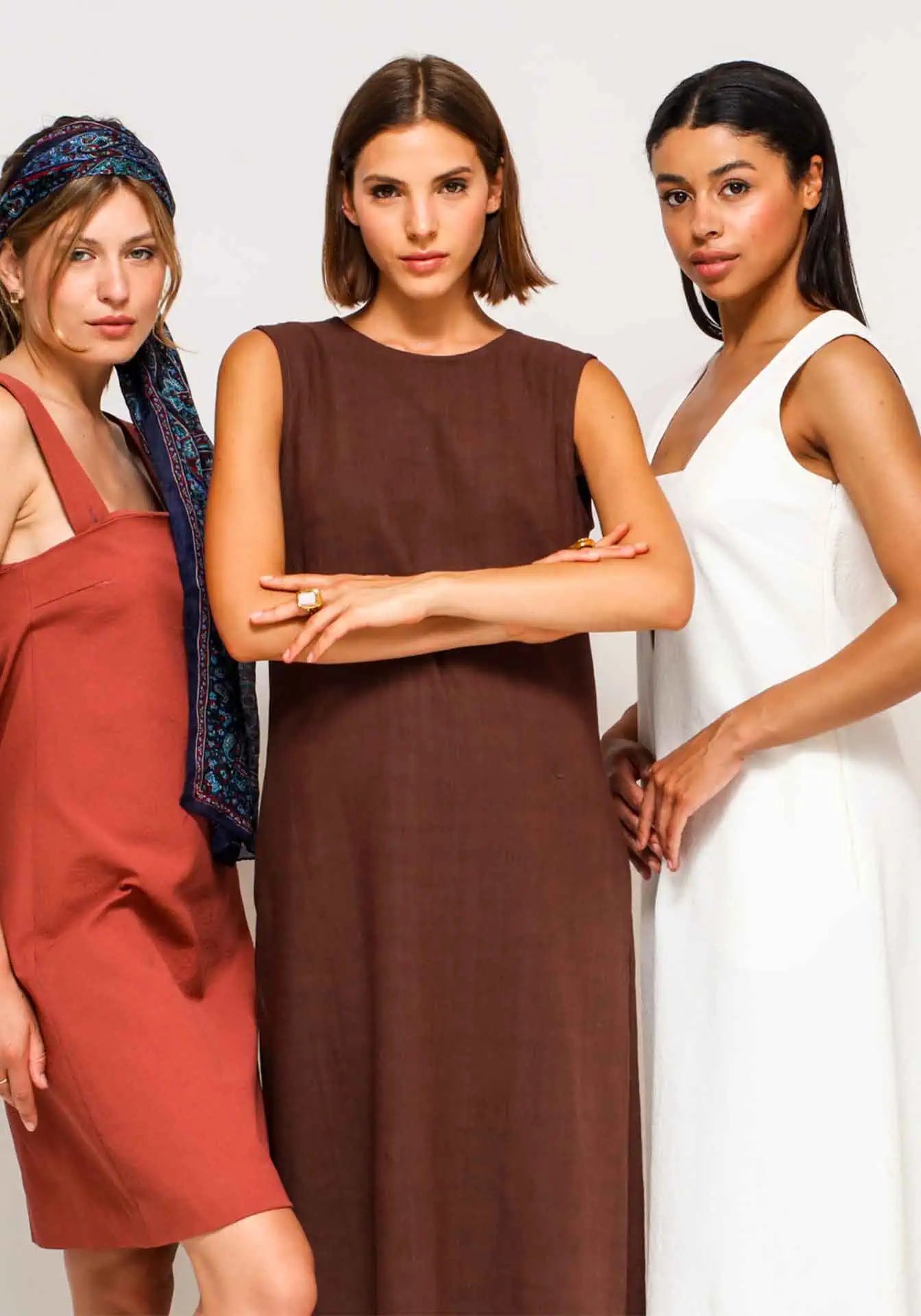 Three women standing with a white summer dress, a brown linen dress and a cotton short dress.