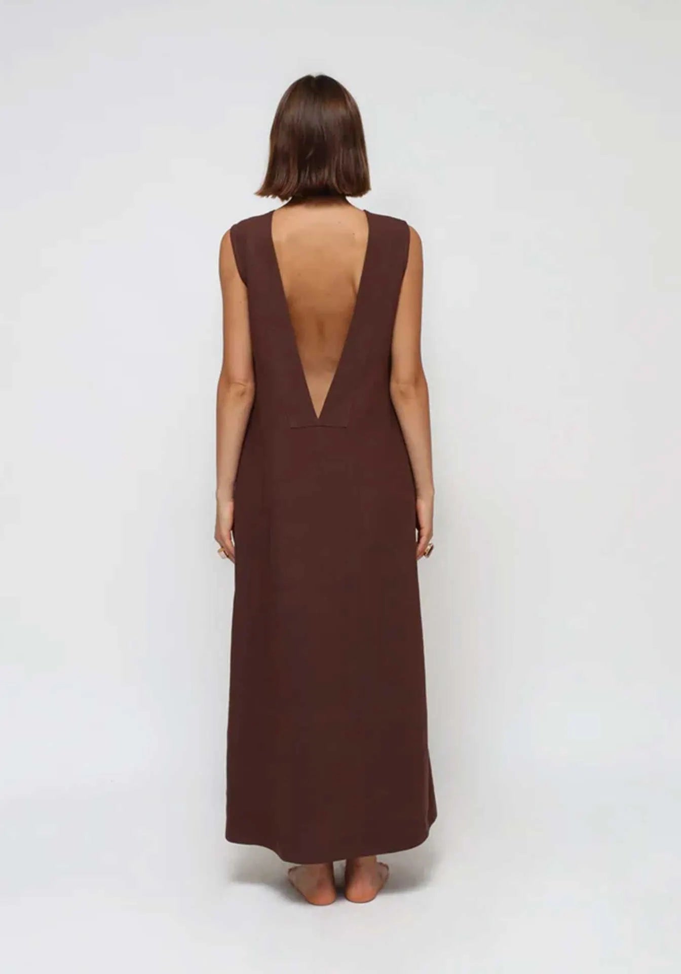 A woman standing from behind with a V-back linen brown Humans & Land dress for summer