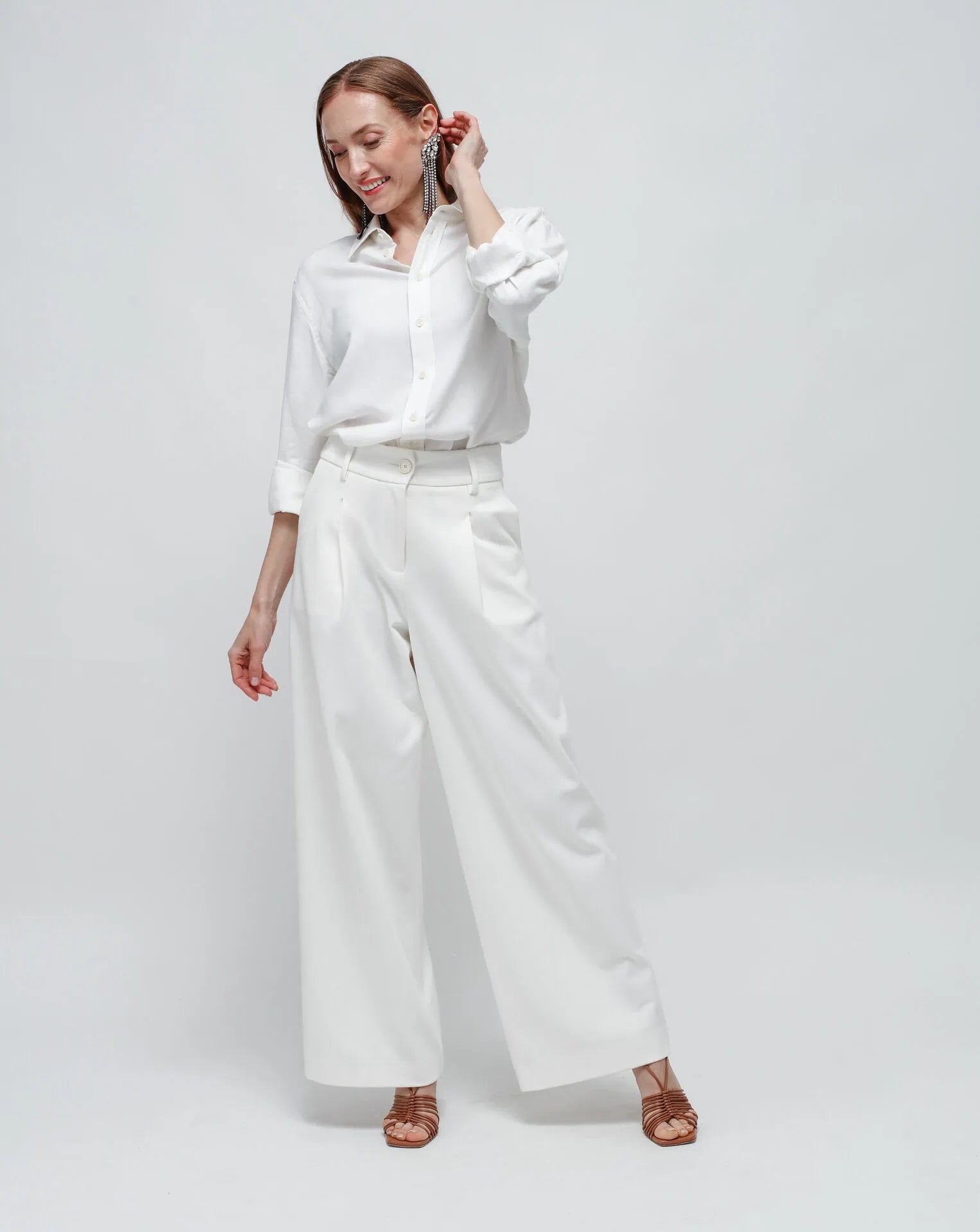 Woman wearing white palazzo pants in Punto Milano (Milano stitch) and matching white boyfriend shirt on a white seamless background.