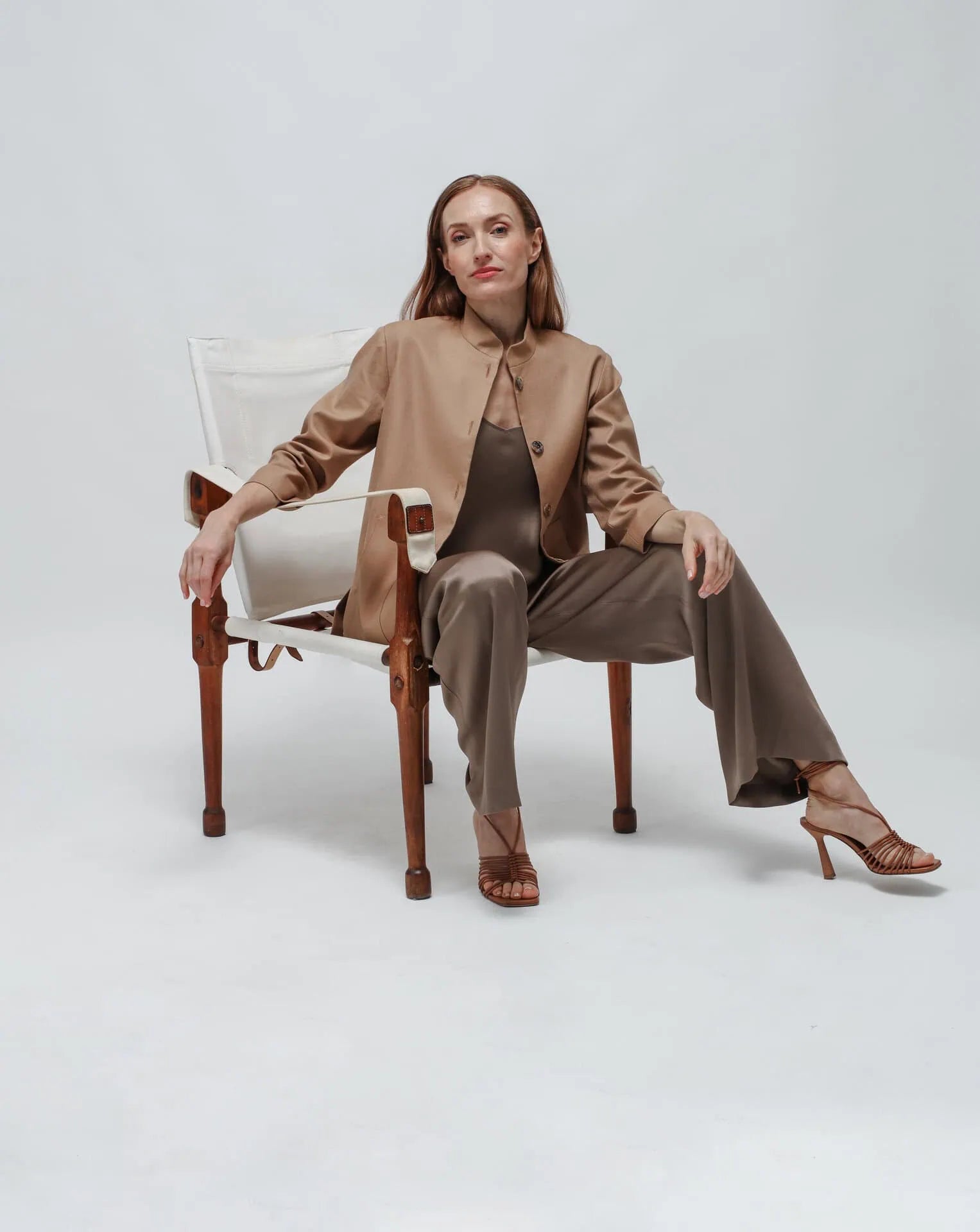 Woman in a brown outfit sitting on a chair against a white background