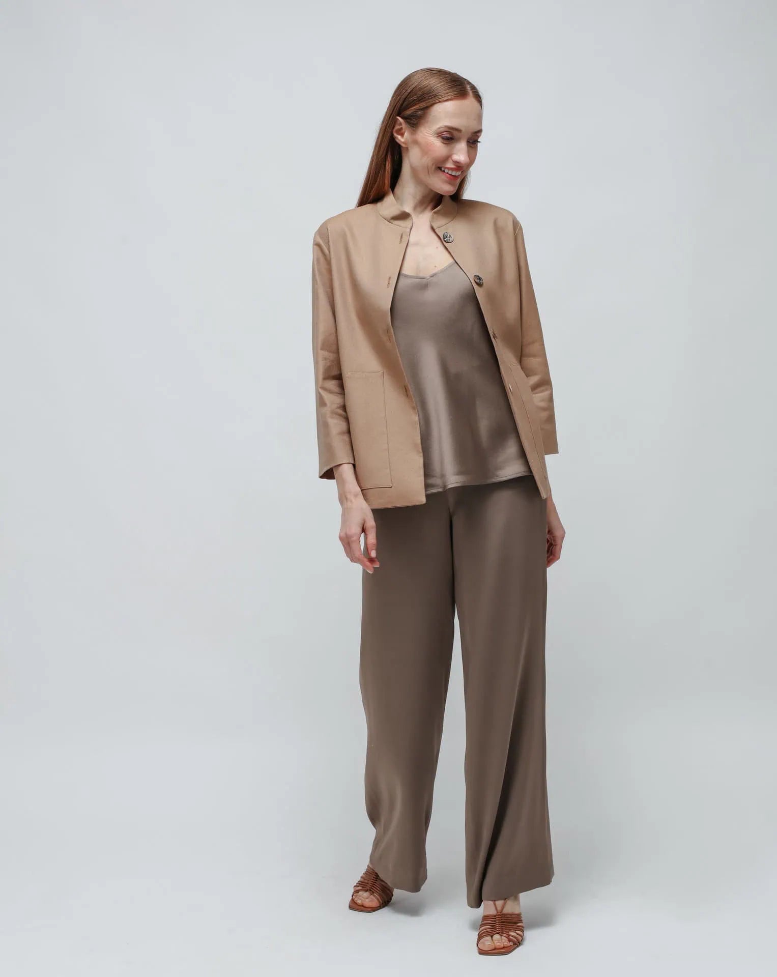 Woman in olive green satin pants and top standing in front of white background.
