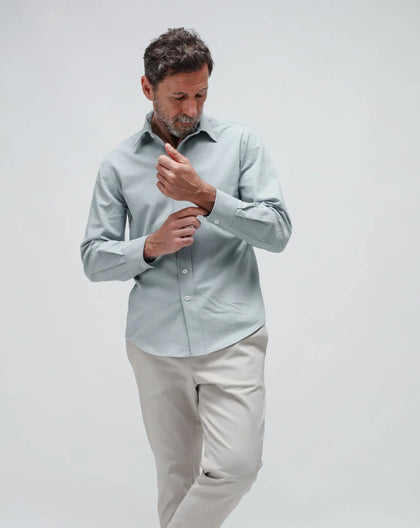 A man wearing a light blue linen shirt with a collar and short sleeves, standing in a relaxed pose.