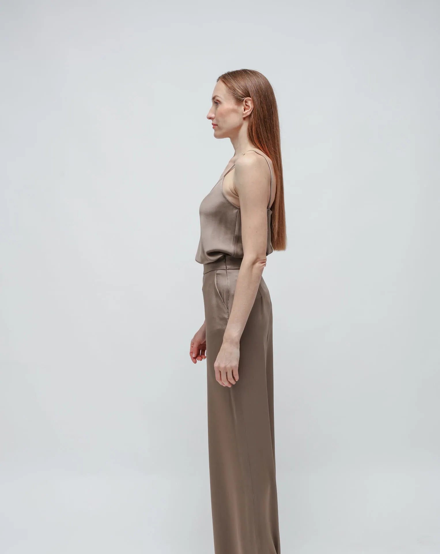 Woman in olive green satin pants and top standing in front of white background.