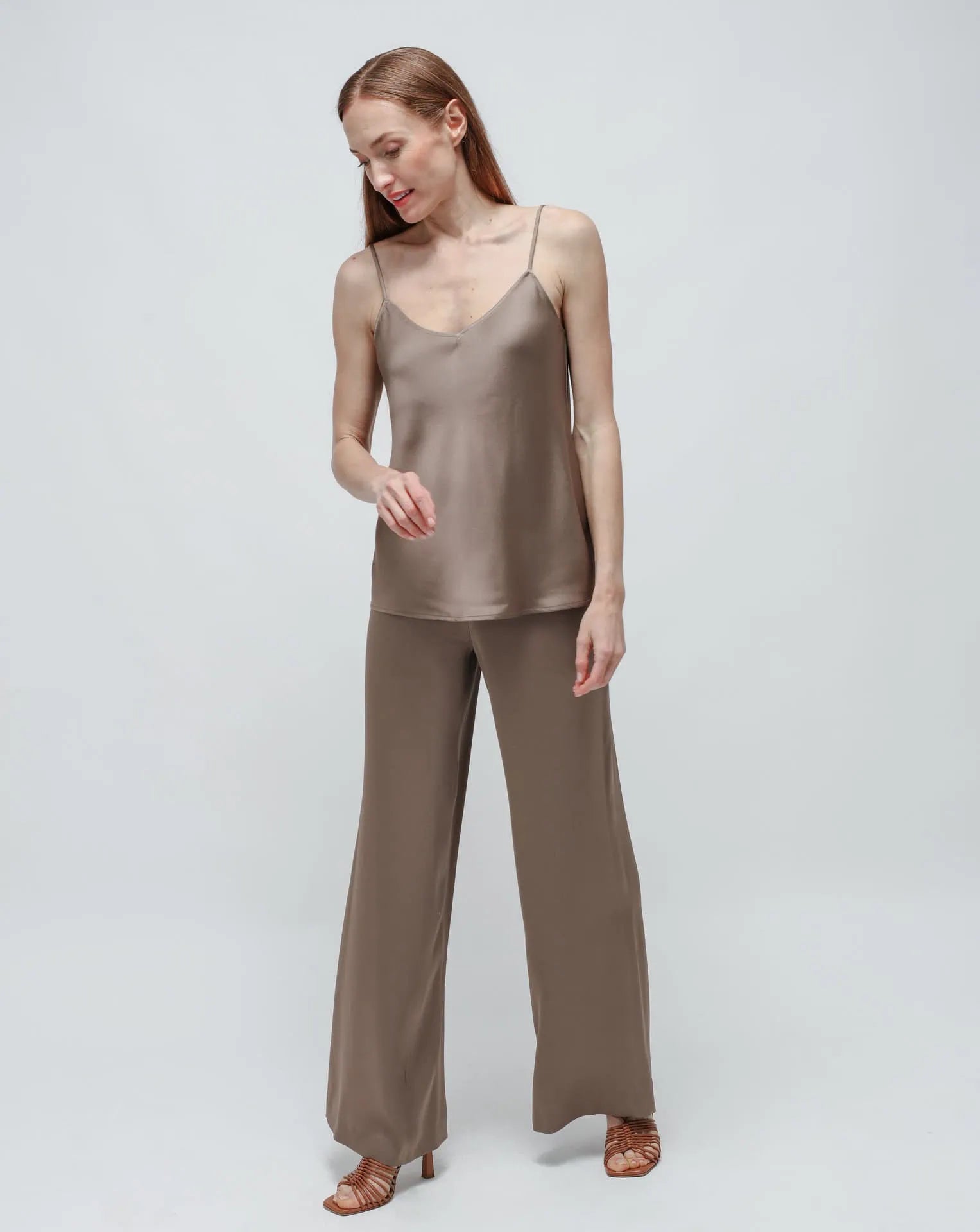 Woman in olive green satin pants and top standing in front of white background.