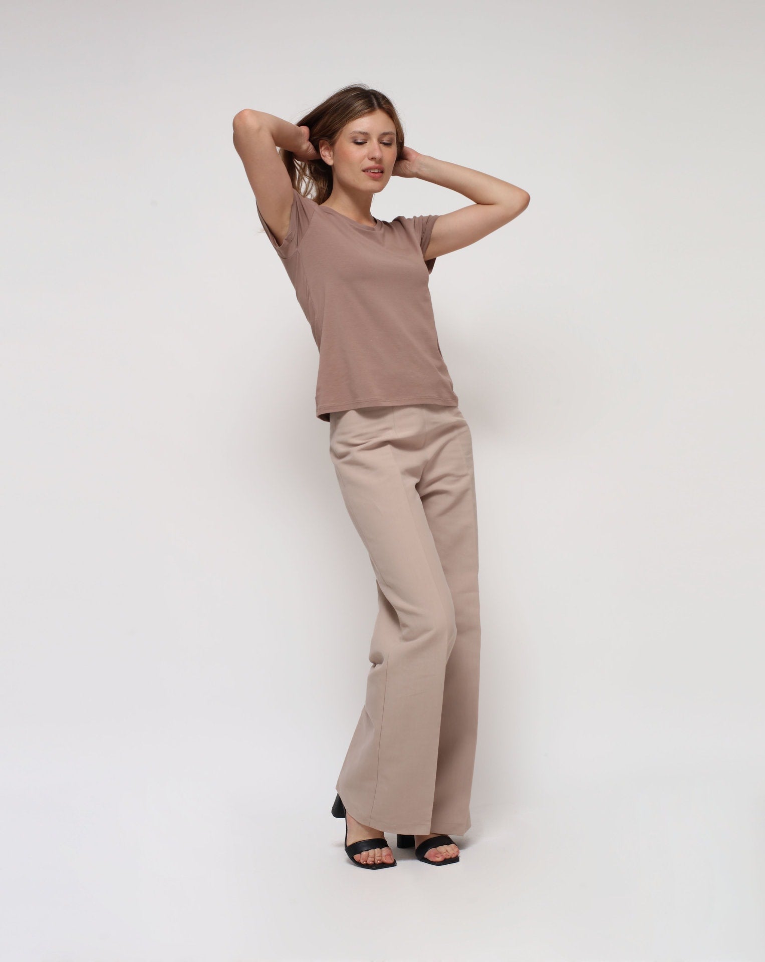 A woman wearing a short-sleeved brown t-shirt and beige pants.