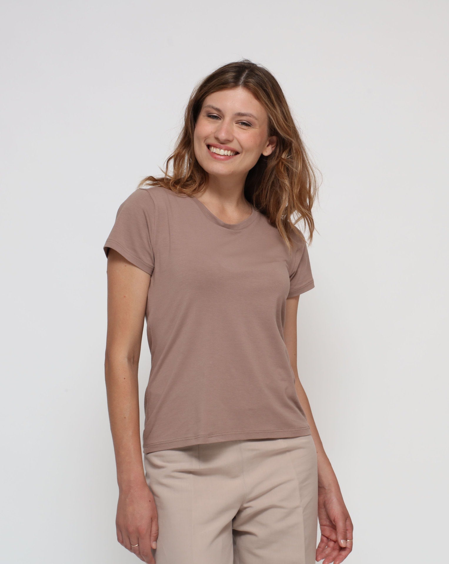 A woman wearing a short-sleeved brown t-shirt and beige pants.