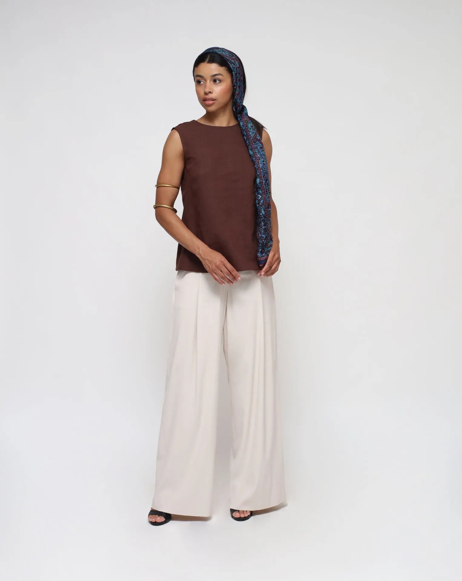 Woman wearing a linen top with V-Back and white palazzo pants in a seamless background.