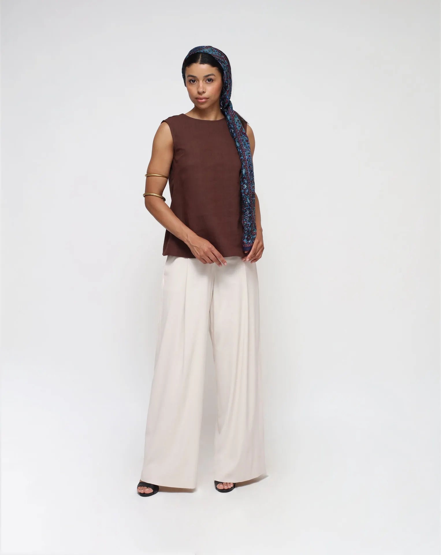 Woman wearing a linen top with V-Back and white palazzo pants in a seamless background.