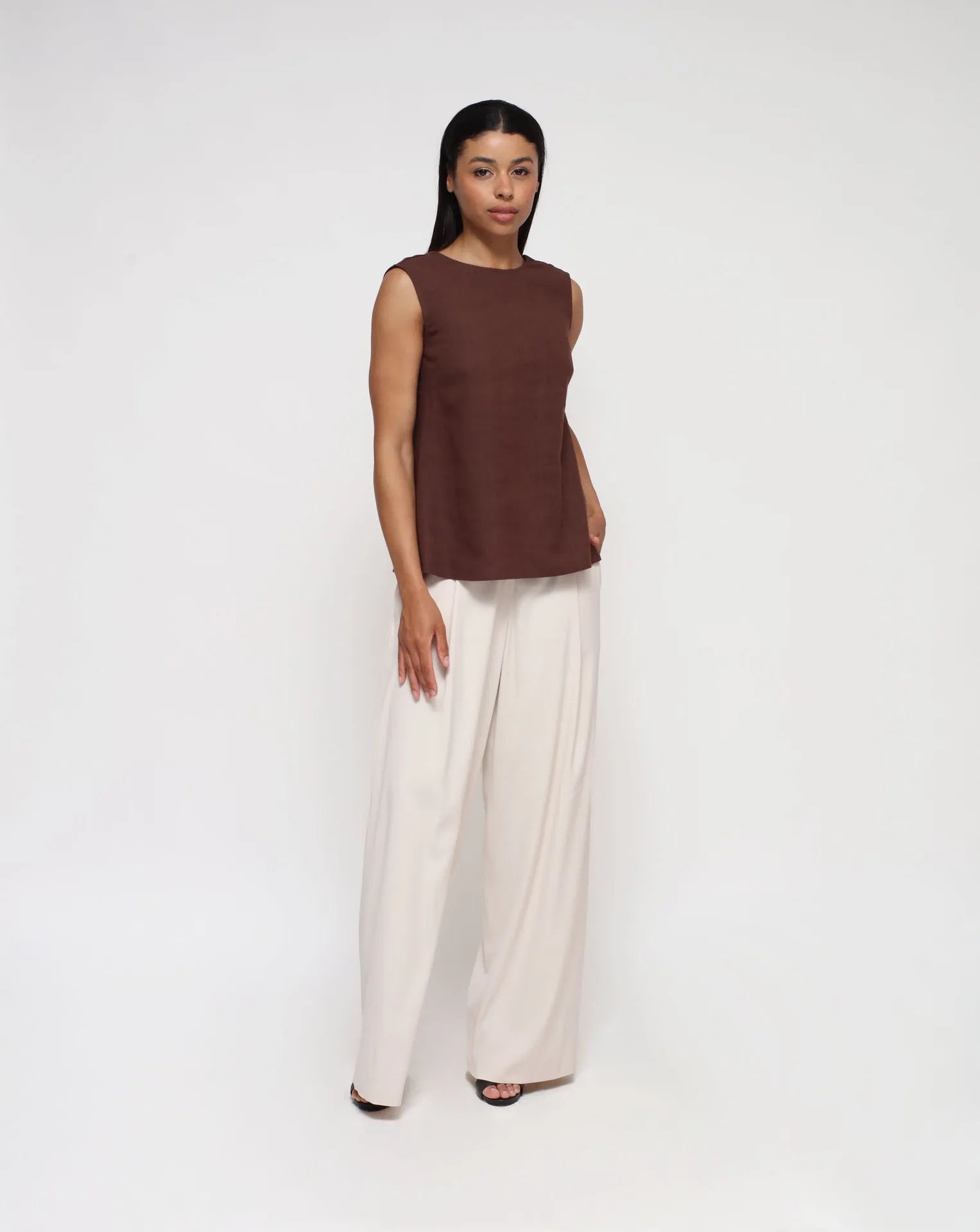 Woman wearing a linen top with V-Back and white palazzo pants in a seamless background.