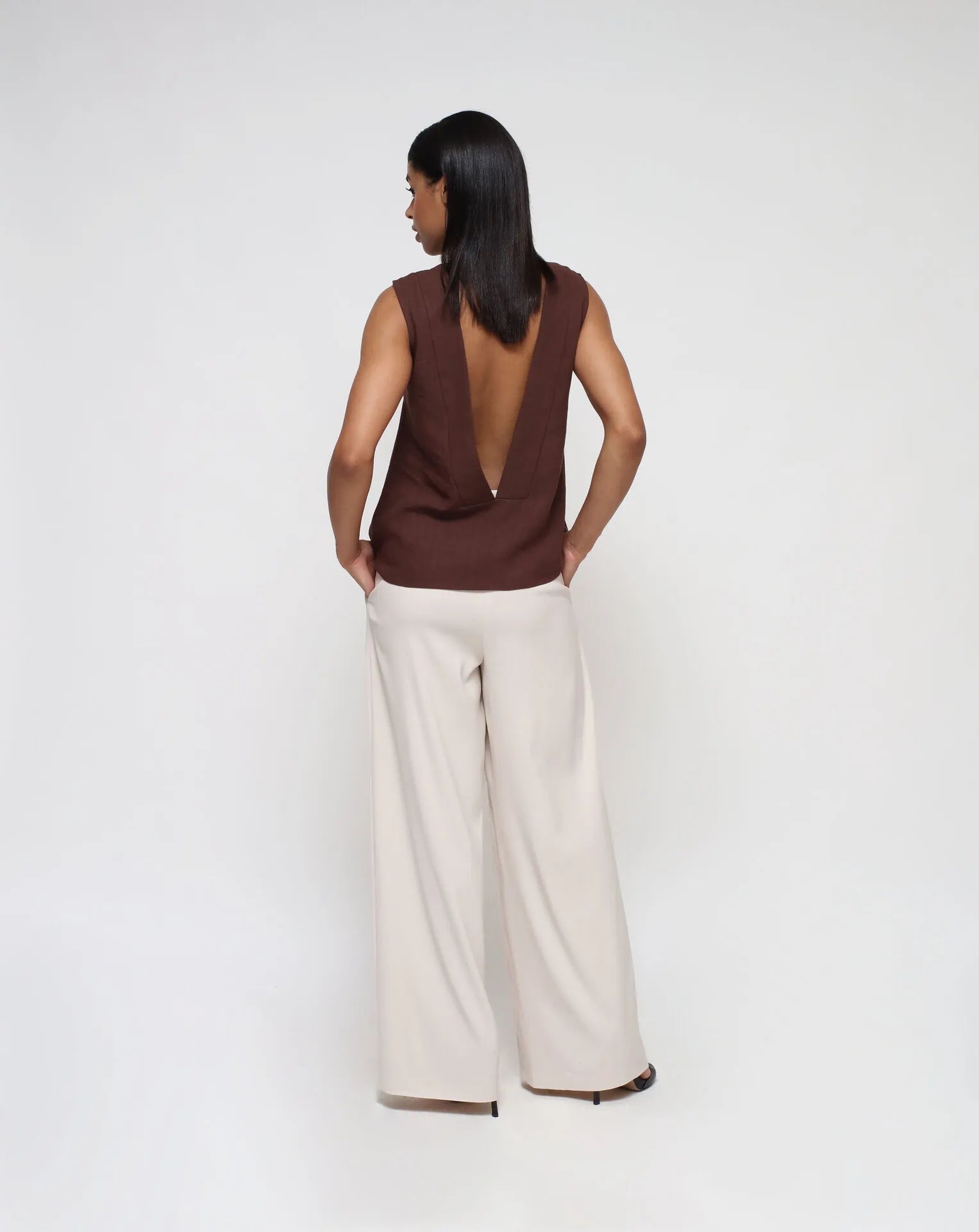 Woman wearing a linen top with V-Back and white palazzo pants in a seamless background.