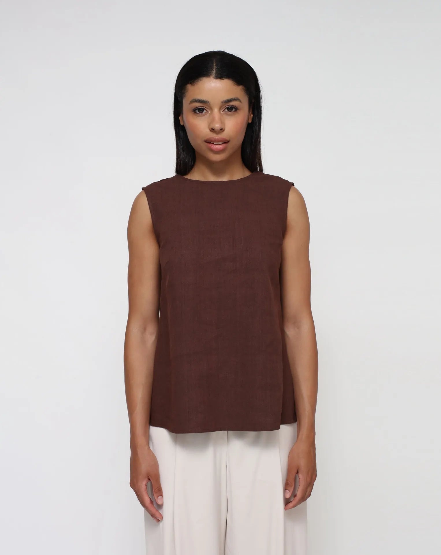 Woman wearing a linen top with V-Back and white palazzo pants in a seamless background.