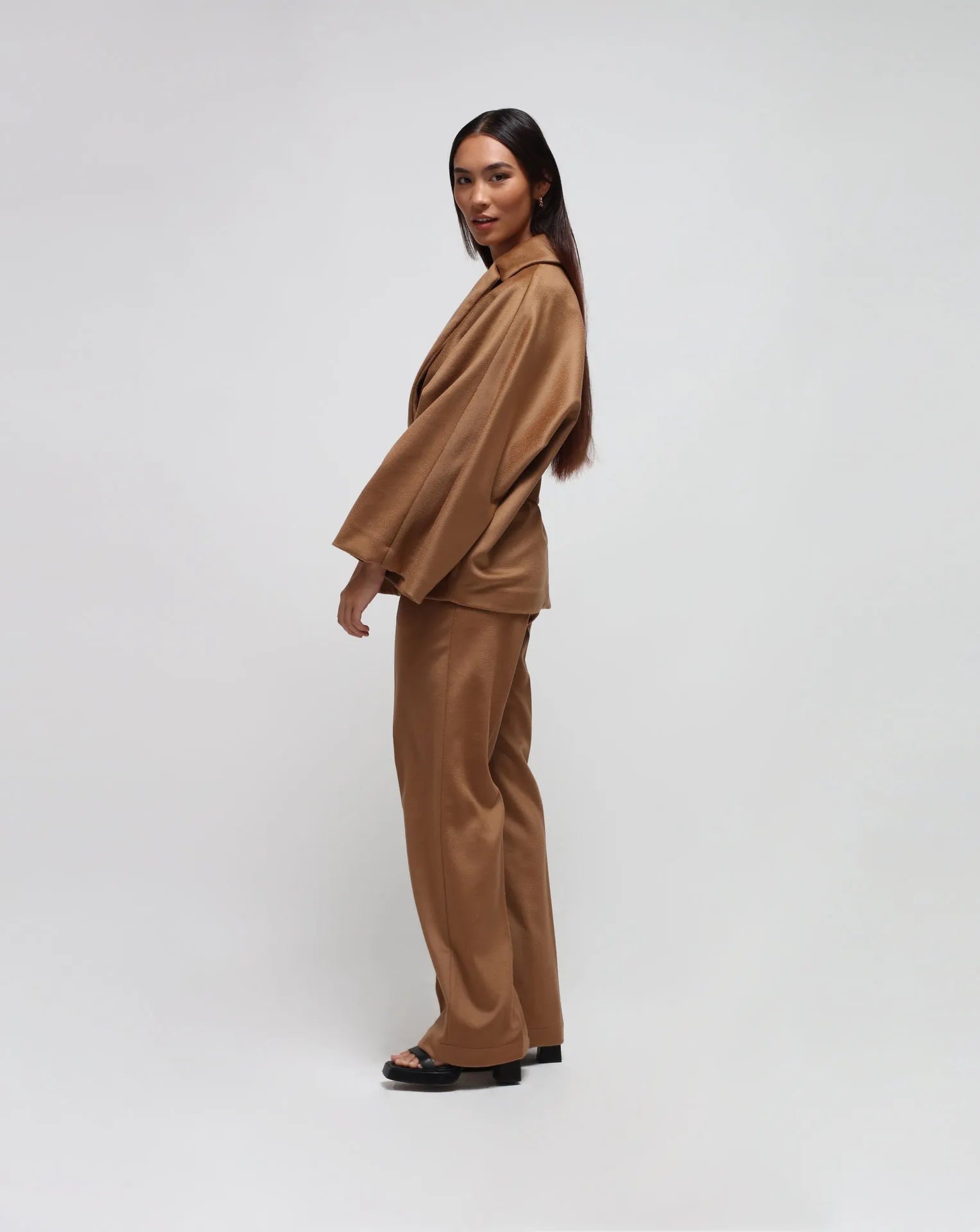 Woman wearing a camel kimono and straight pants on white seamless background.