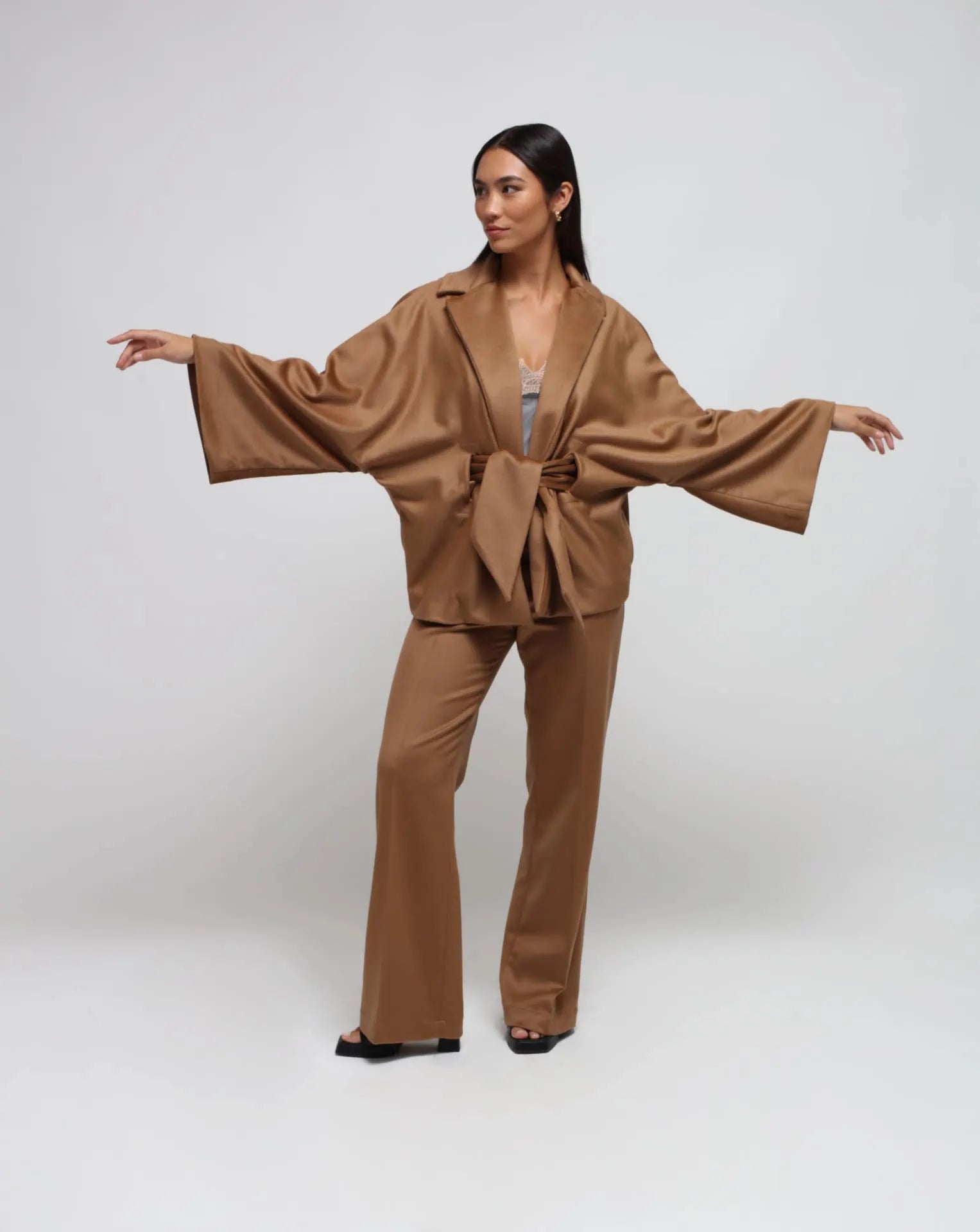 Woman wearing a camel kimono and straight pants on white seamless background.