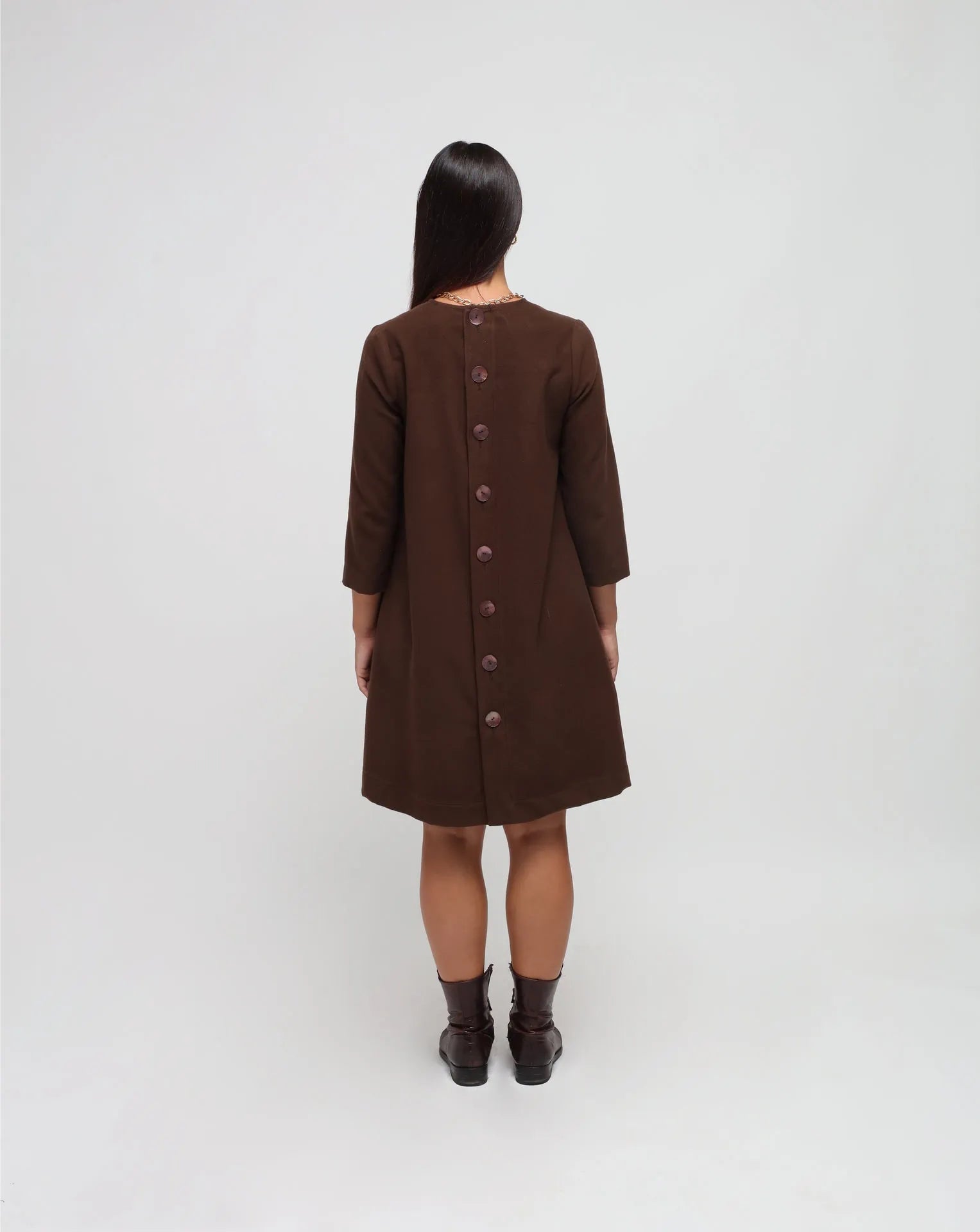 Woman in white background with brown flared dress in brown.