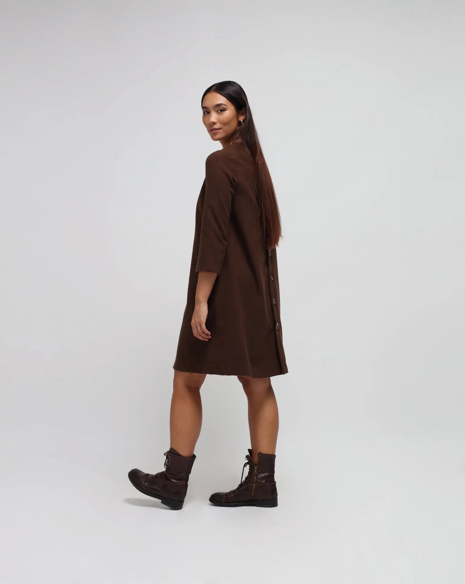 Woman in white background with brown flared dress in brown.