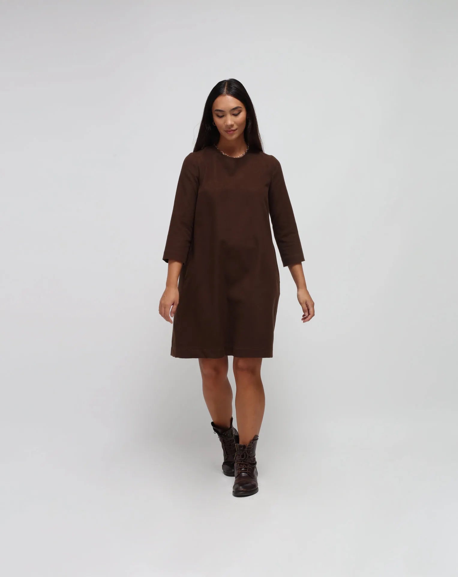 Woman in white background with brown flared dress in brown.