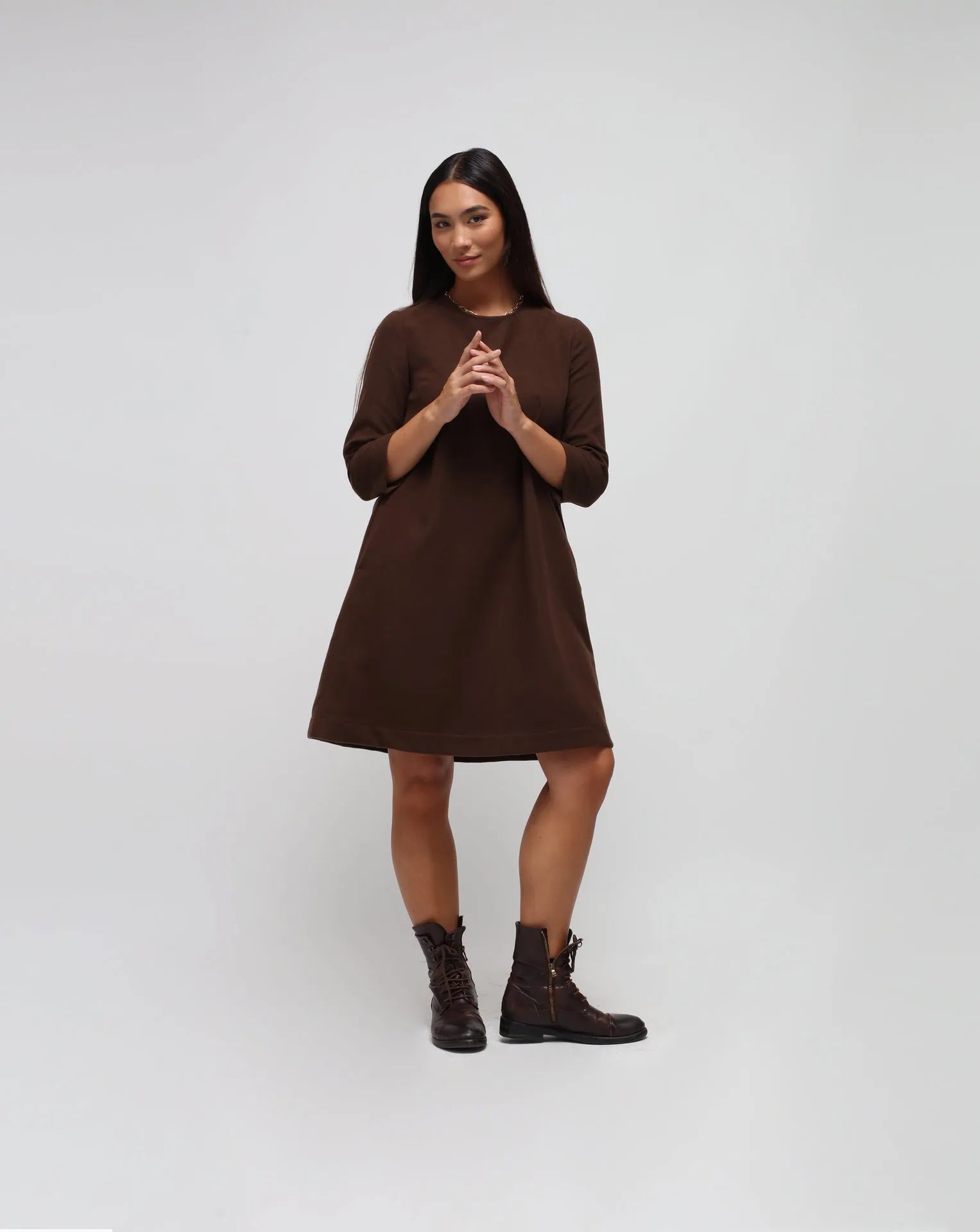 Woman in white background with brown flared dress in brown.