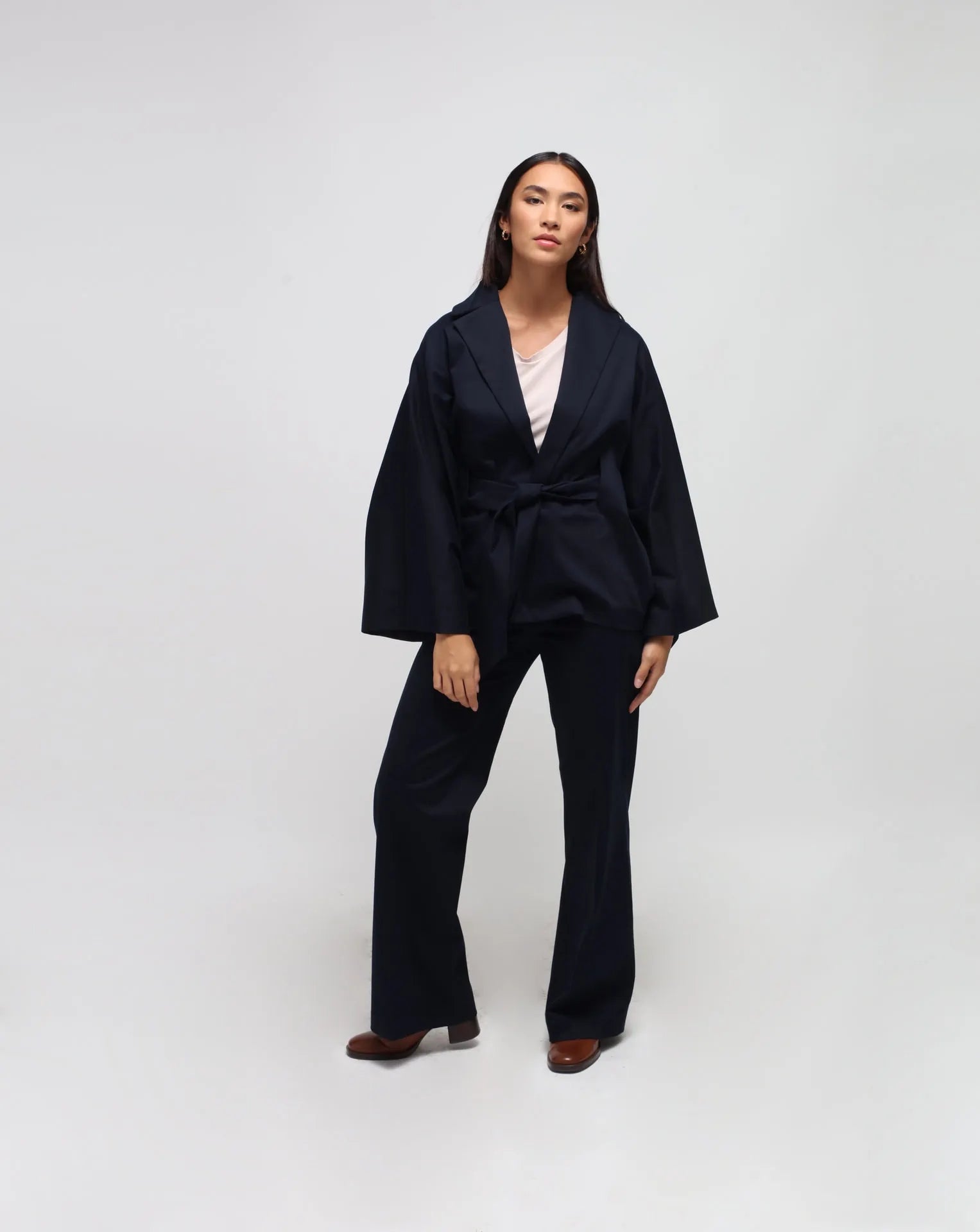 A person standing against a plain background, wearing blue straight pants with side pockets. They are also wearing a beige-colored top.