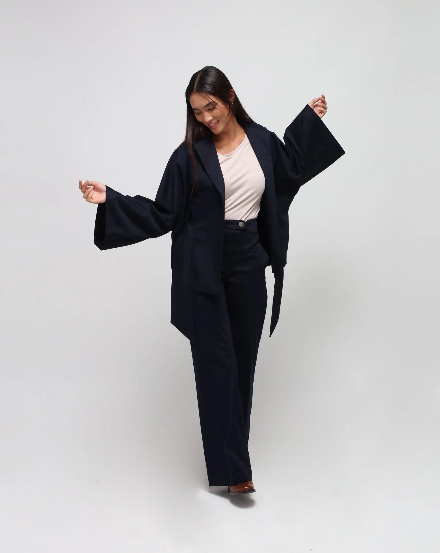 A person standing against a plain background, wearing blue straight pants with side pockets. They are also wearing a beige-colored top.