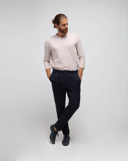 A man standing, wearing a beige t-shirt and blue traveller pants in cupro. The pants have a dropped crotch and drawstring.