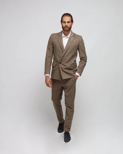 A male model wearing a beige double-breasted suit with traveller's pants, standing against a white background.