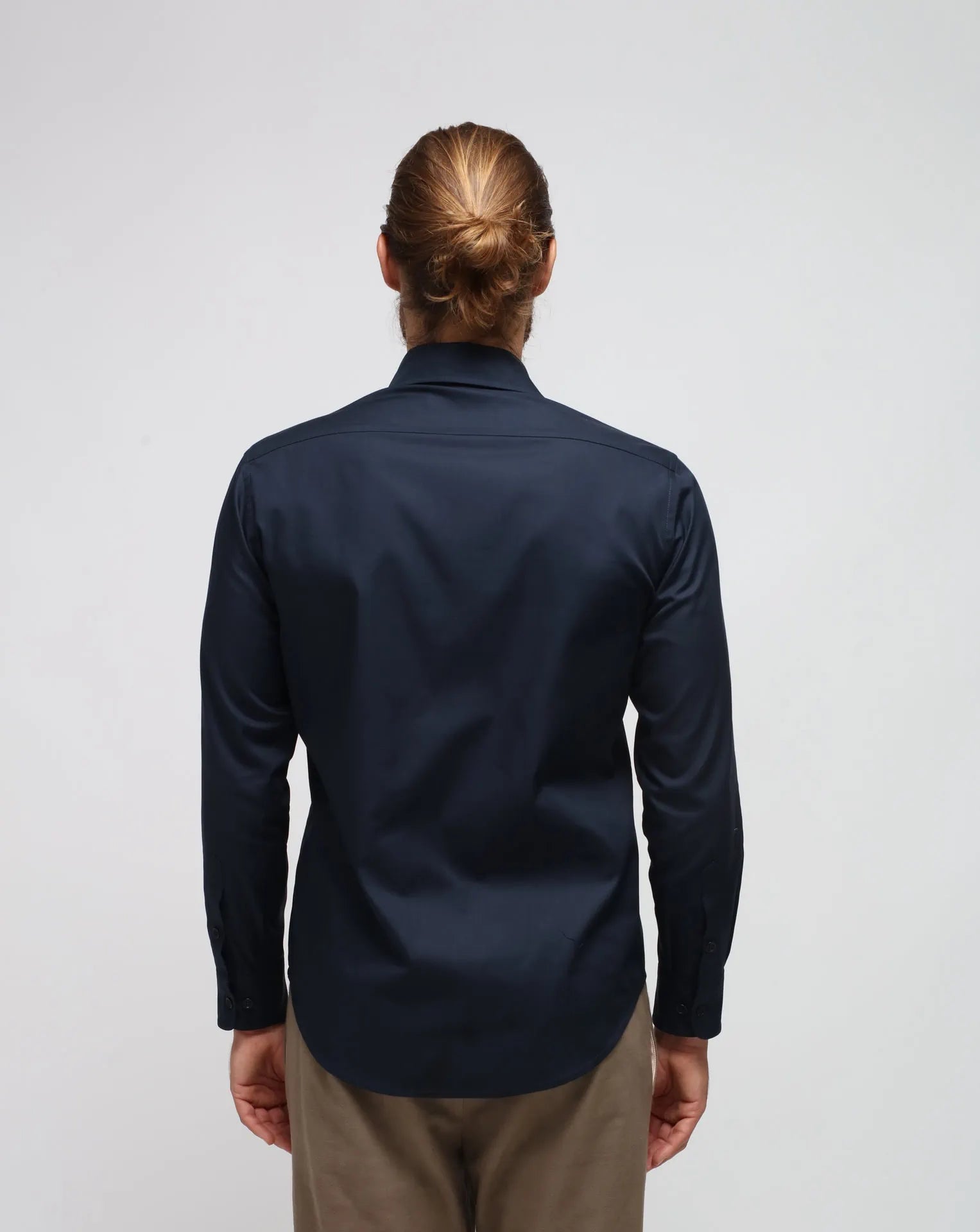 A man wearing a cotton blue shirt with brown pants standing in white seamless background.