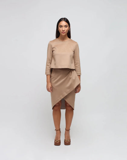 A woman wearing a beige pencil skirt with a tulip shape, paired with a beige top and brown shoes. The skirt is at a midi length.