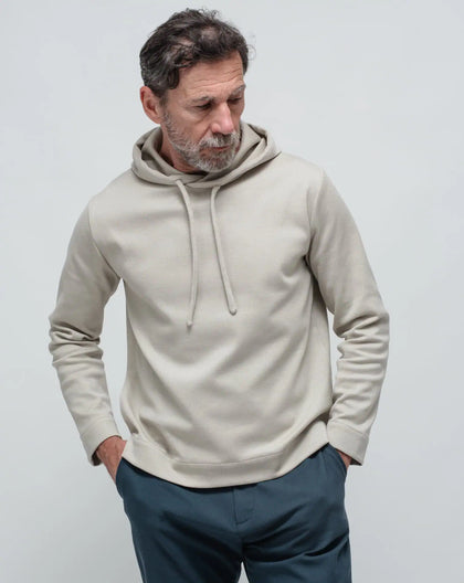 A man wearing a beige Punto Milano hoodie with a hood, looking to the side.