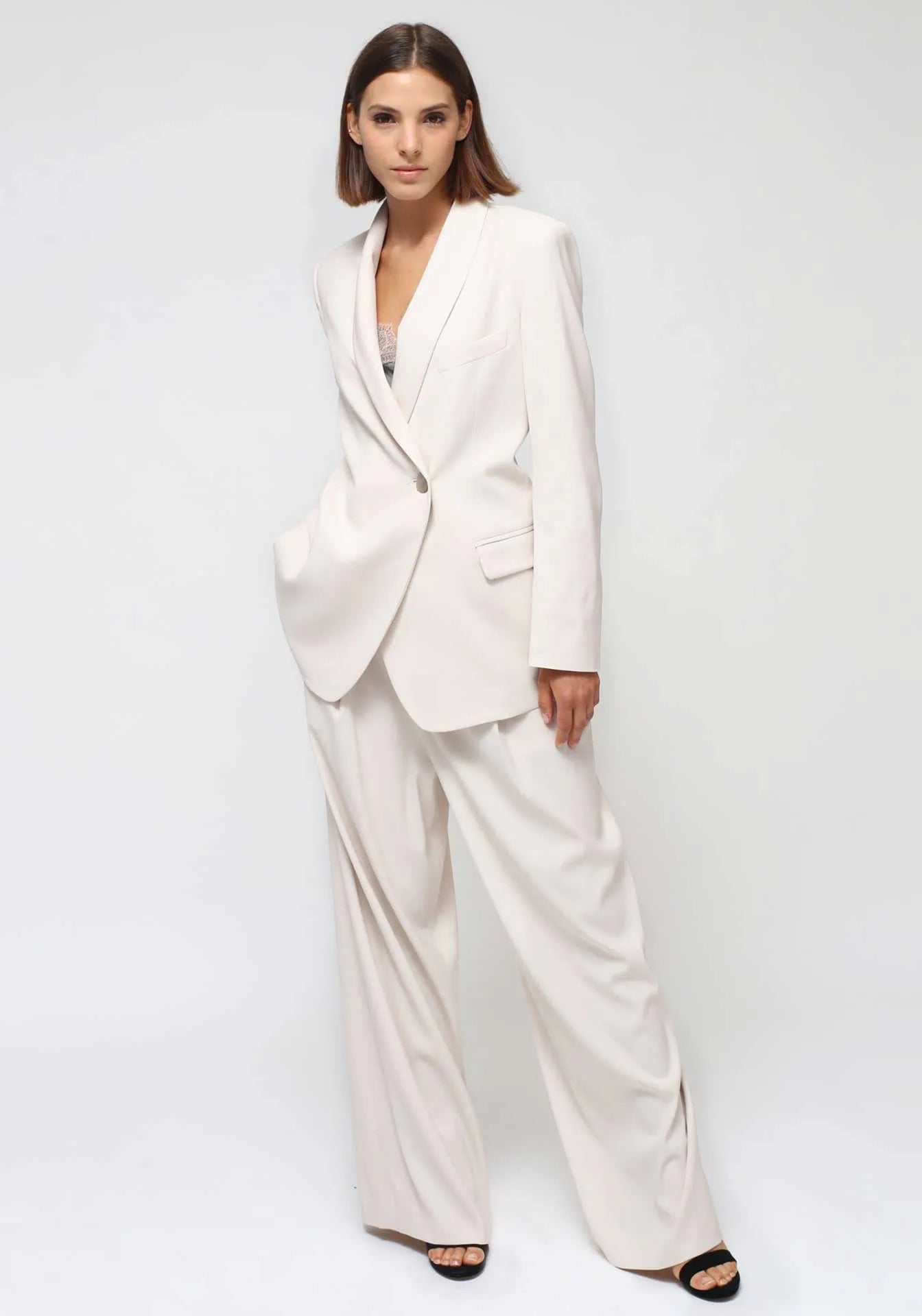 A woman standing with her hand in the pocket wearing a white summer tailleur from Humans & Land (H&L) on white background.