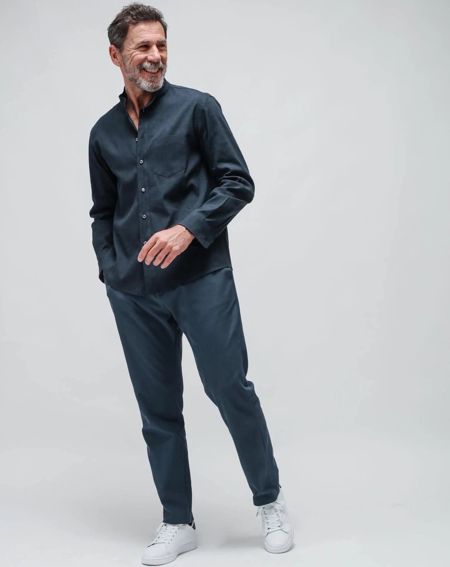 A man wearing a blue pair of straight pants in gabardine and blue linen Korean shirt on a white seamless background.