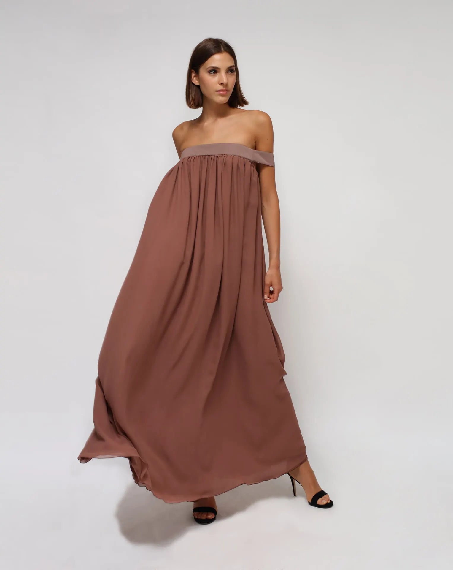 A woman with a silk chiffon brown strapless summer dress on a white seamless background..