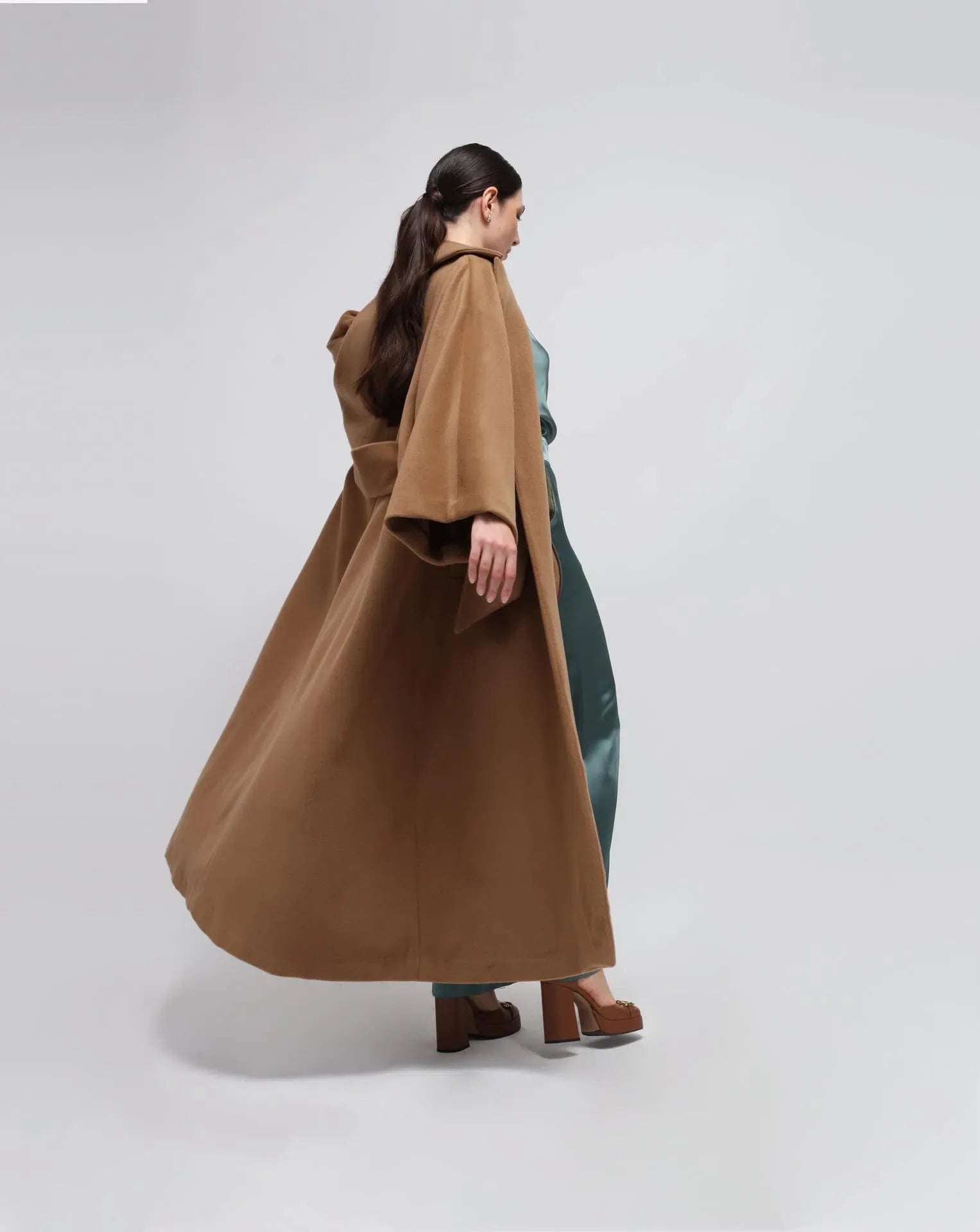 A woman wearing a camel wool Kimono long coat on a white seamless background.