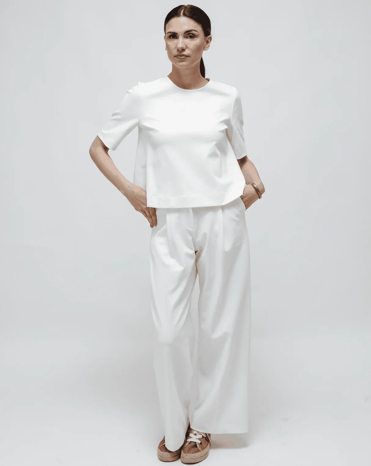 A woman with a white Punto Milano Top and palazzo pants on a white seamless background.
