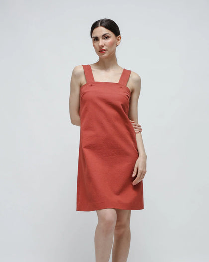 A woman wearing an orange flared cotton dress with a side zipper and adjustable straps.