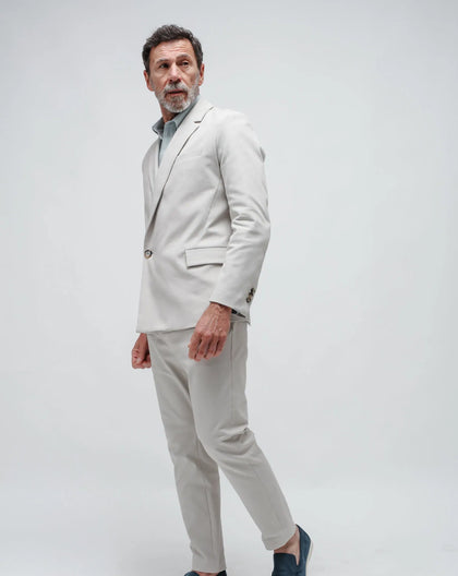 A man wearing a beige double-breasted summer jacket with a single button on a white seamless background.