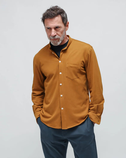 A men wearing a mustard Korean shirt-jacket and blue gabardine pants on a white seamless background. 