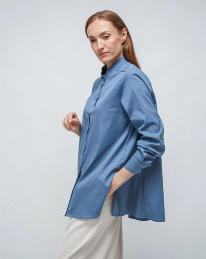 A woman wearing a light blue long-sleeved Korean shirt with a flared design, paired with white trousers.
