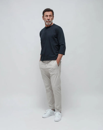 A man standing with white gabardine summer pants and a blue t-shirt on a white background.