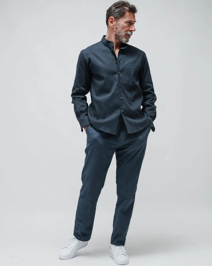 A man standing wearing a blue linen Korean shirt with a collared neckline, paired with white sneakers.