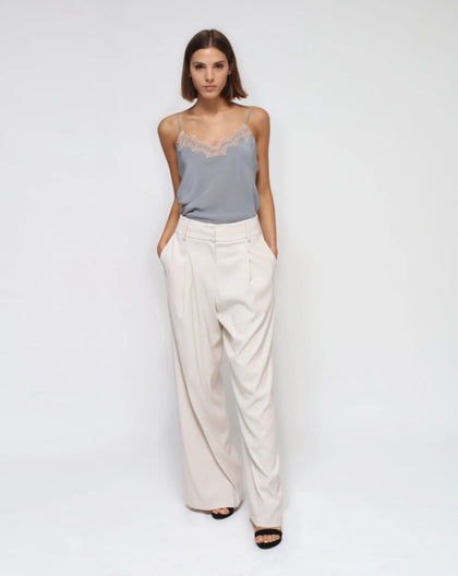 A model wearing white pleated palazzo pants with front pockets and a high waist, paired with a gray top and black shoes.