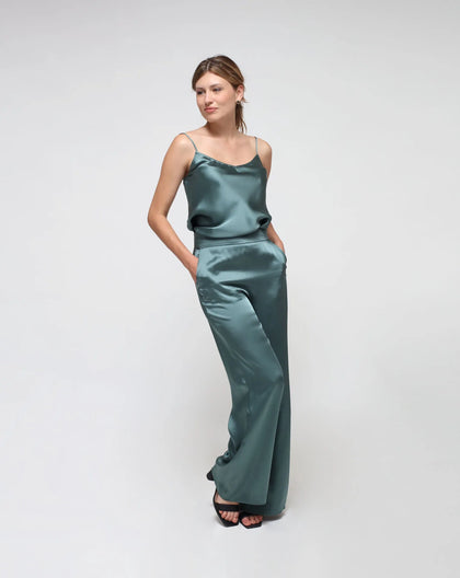 A model wearing high-waisted, flared green satin pants with a side zipper, standing against a neutral background.