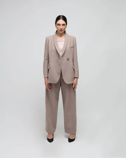 A model wearing a grey double-breasted, oversized wool jacket with a single button, shawl lapel, and pockets with flaps.