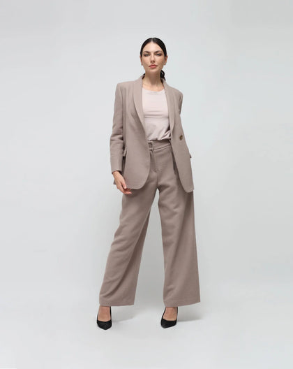A woman standing against a white background, wearing a grey wool one-button jacket and grey wool palazzo pants.