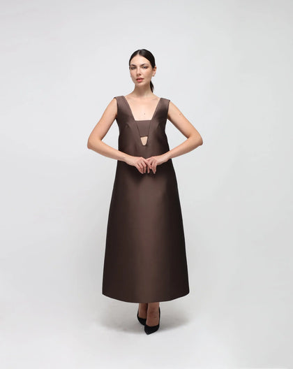 A woman modeling an ankle-length brown evening dress with large shoulder straps and a V-shaped front and back.