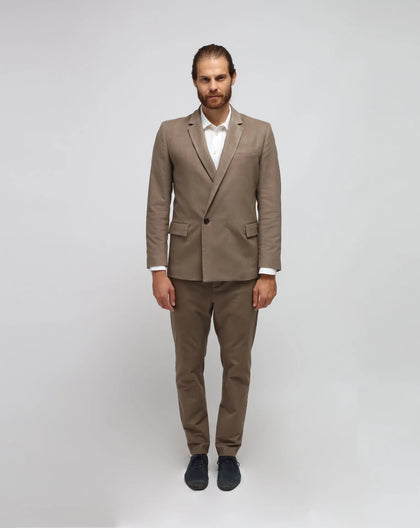 A man standing against a white background, wearing a beige double-breasted jacket with a one-button front, paired with matching trousers.