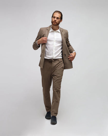 A man wearing beige traveller pants with a jacket and a white shirt, standing against a white background.