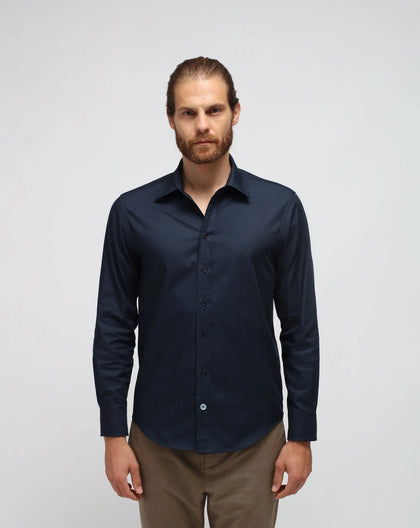 A man wearing a cotton blue shirt with brown pants standing in white seamless background.