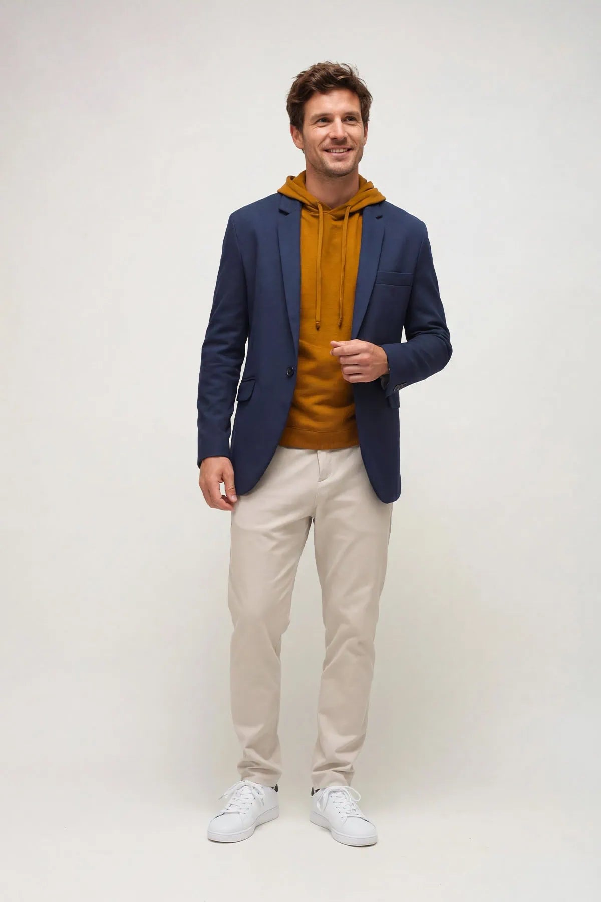 A man wearing a gabardine blue jacket and beige traveler pants on white seamless background.