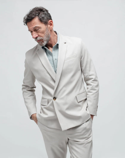 A man wearing a beige double-breasted summer jacket with a single button on a white seamless background.